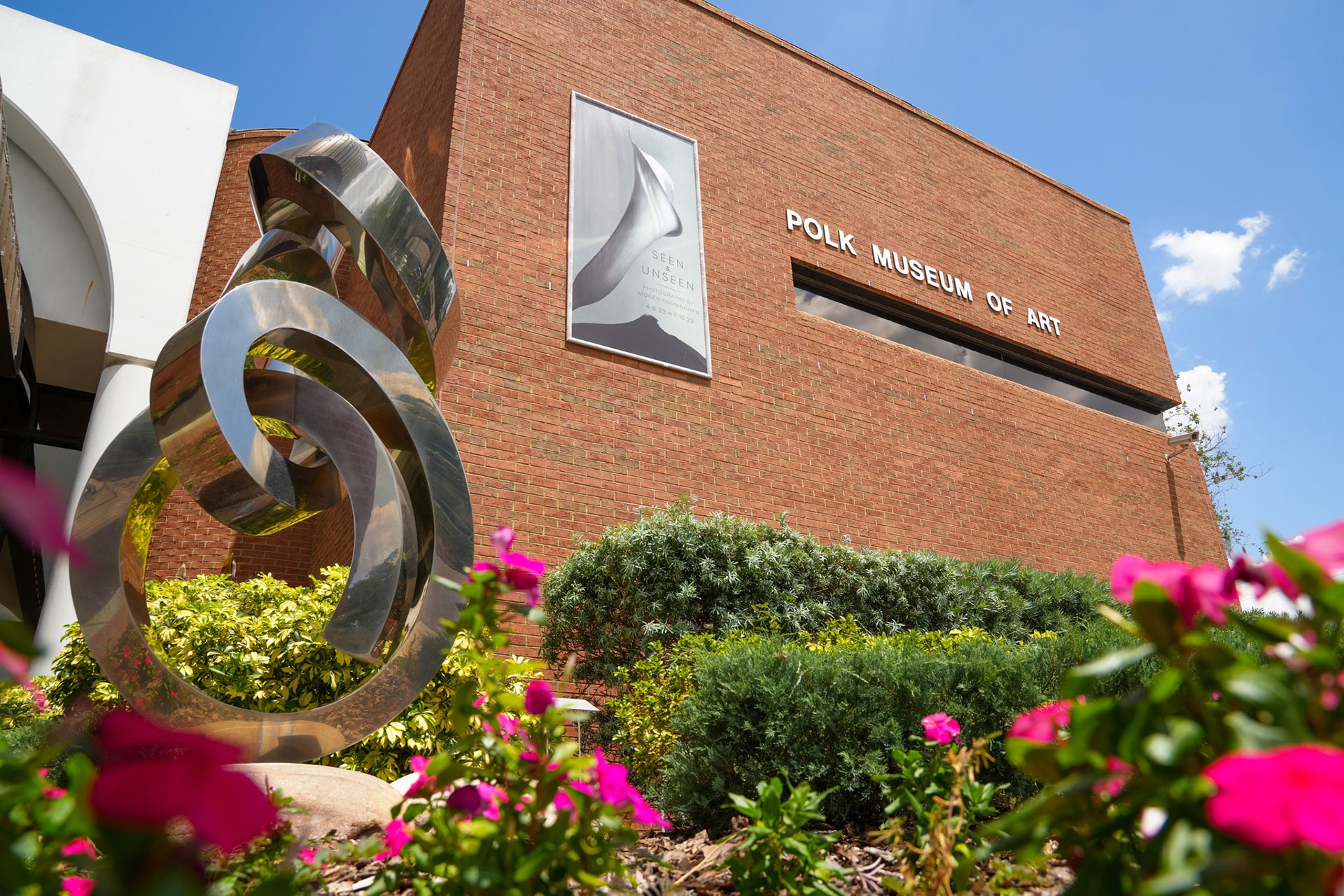 Exterior of Polk Museum of Art building with metal sculpture and pink flowers in frame.